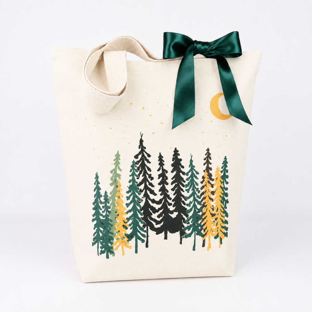 An off-white canvas tote bag with a dark green satin bow and a forest tree print in green, black, and yellow, set against a plain white background.
