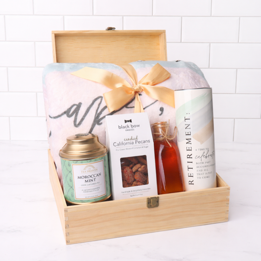 Gift basket with tea, snacks, and a blanket in a wooden box on a white background