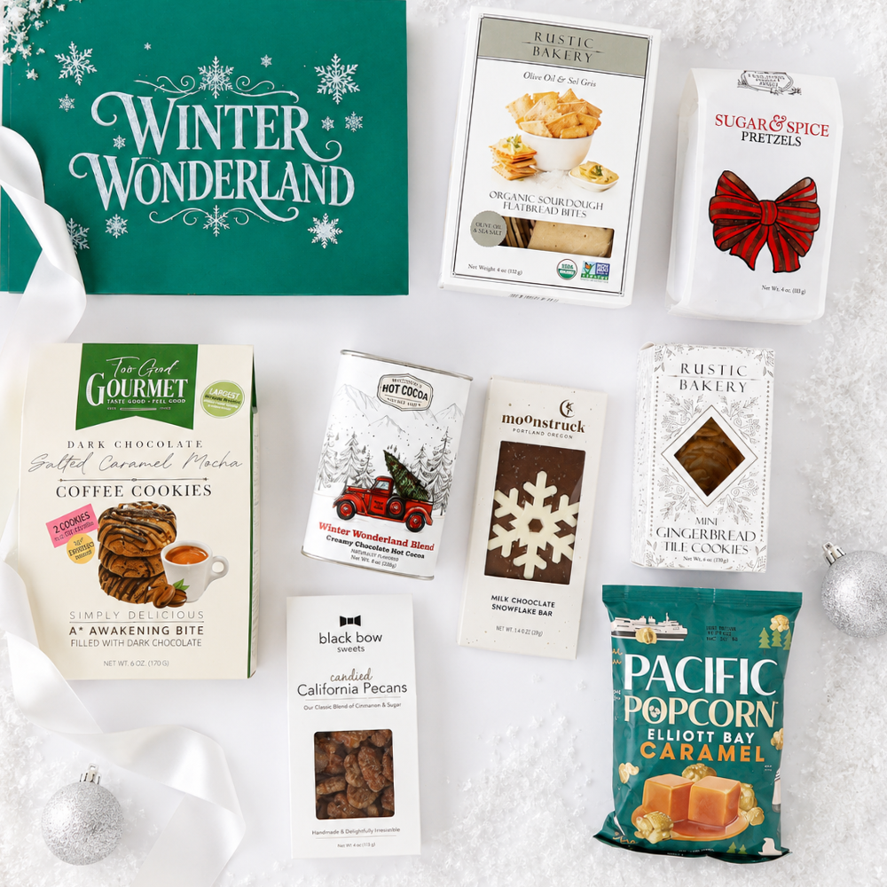 A curated holiday gift assortment featuring a green 'Winter Wonderland' box, a bag of Pacific Popcorn, a box of Rustic Bakery Pretzels, and several individually wrapped gourmet snacks arranged on a white textured surface with silver ornaments.